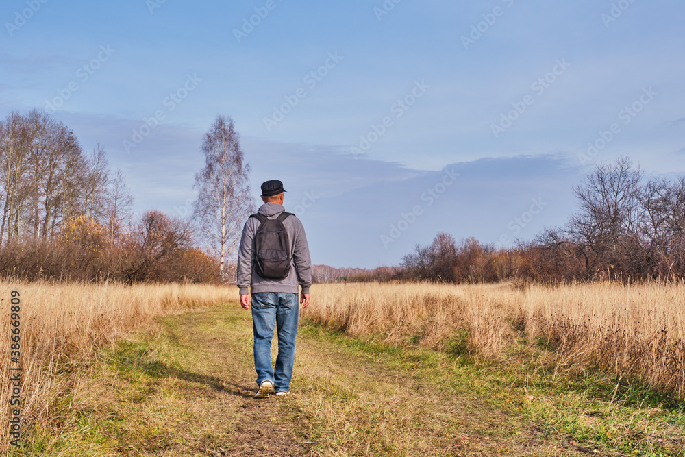 Active man in casual with backpack is walking in a meadow late autumn. Siberia, Russia.