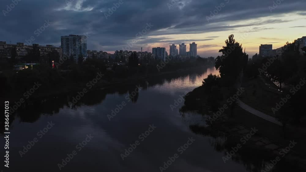 Aerial view of city after rain and water canal near high-rise buildings, evening cloudy sky, avenue with busy traffic behind trees Aerial view of city after rain and water canal near high-rise buildings, evening cloudy sky, avenue with busy traffic behind trees