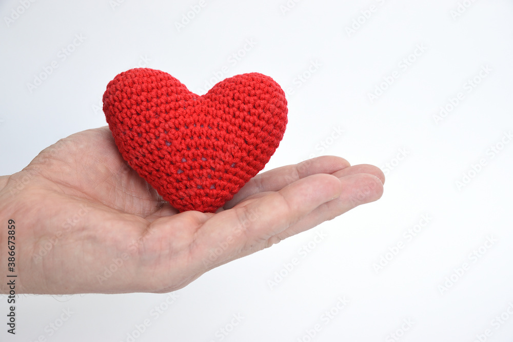 A man's hand holds out a heart knitted of red yarn on the palm A man's hand holds out a heart knitted of red yarn on the palm