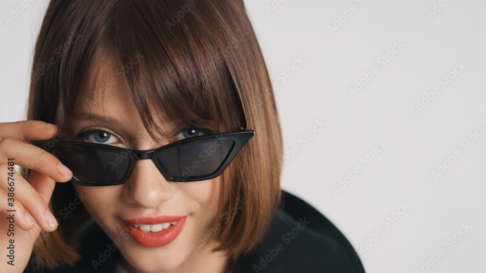 Close up blue eyed girl with bob hair and red lips wearing sunglasses confidently looking in camera isolated on white background Close up blue eyed girl with bob hair and red lips wearing sunglasses confidently looking in camera isolated on white background