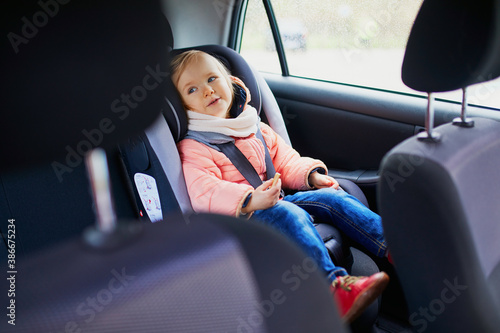 Adorable toddler girl in modern car seat eating cookie
