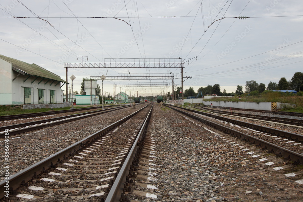 Russian 1520 mm empty railway tracks in perspective and station house, railroad landscape on a cloudy summer day