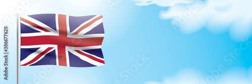 UK flag waving on a blue sky background. Patriotic vector banner design, with the national flag of the United Kingdom, hanging on a sunny background with white clouds. Great Britain flag banner.