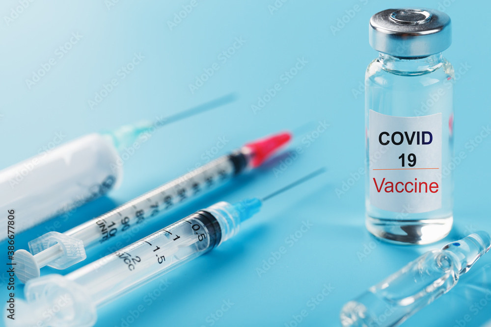 A set of ampoules with the inscription Covid-19 vaccine and a set of syringes against a blue background. A set of ampoules with the inscription Covid-19 vaccine and a set of syringes against a blue background.