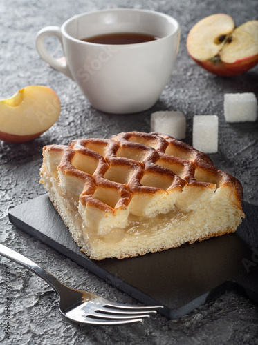 Apple pie on a dark background with apples. A piece of Apple pie on a Board with a fork and tea in the background.