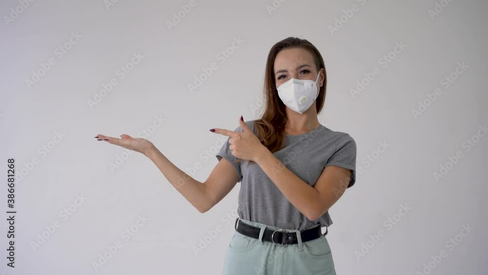 Young woman with hand aside pointing an empty blank space and wearing medical face mask. Copy space and white background. Frontal view. Young woman with hand aside pointing an empty blank space and wearing medical face mask. Copy space and white background. Frontal view.