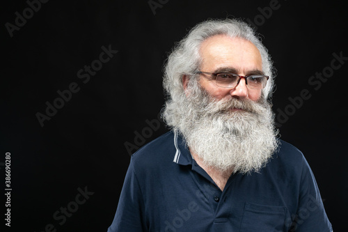 A man with gray hair and a beard. Grandfather with glasses. Portrait of an elderly man on a dark background. A thoughtful man with a friendly smile.