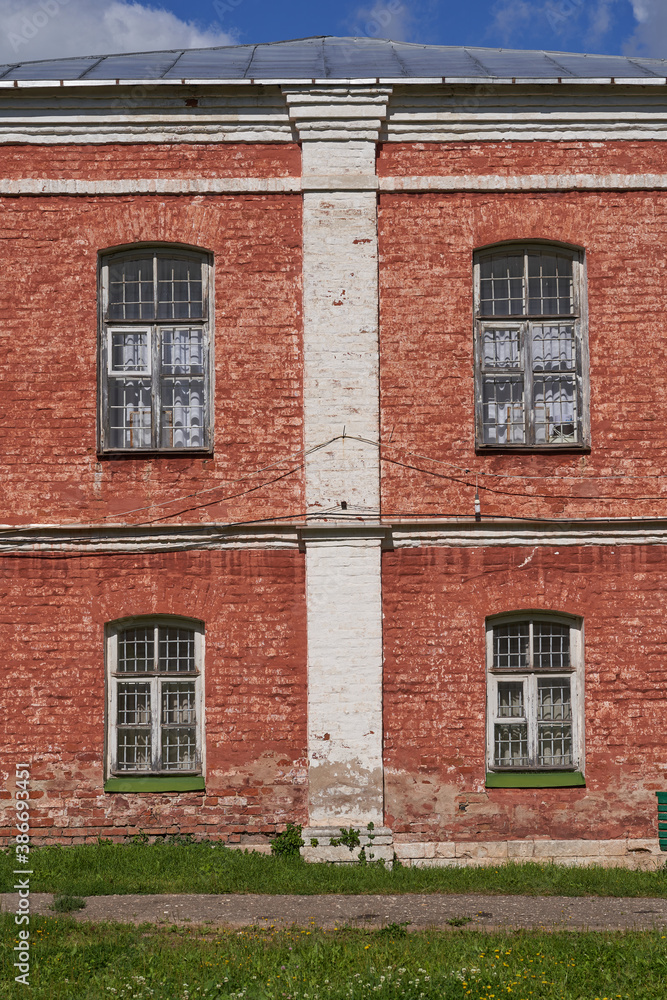 Brick facade of an old building with four Windows and a metal roof