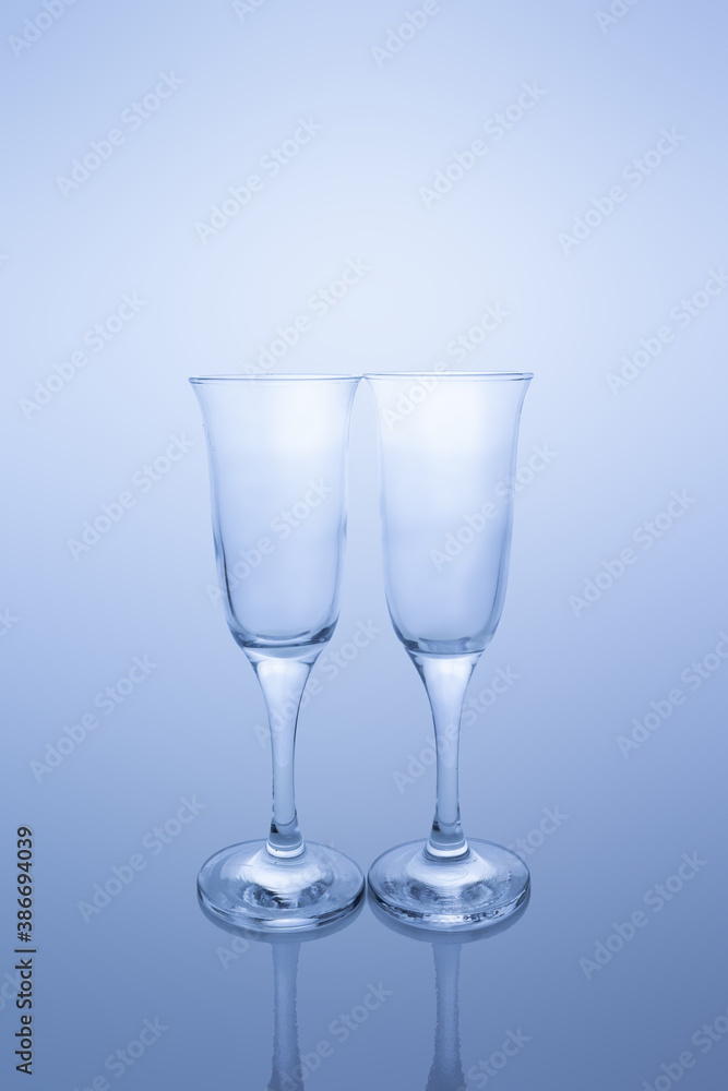 Two empty transparent glass goblets on reflective surface in blue tint Two empty transparent glass goblets on reflective surface in blue tint