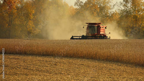 Front of red combine harvesting soybeans in a dusty field in late afternoon in the Midwest; USA
