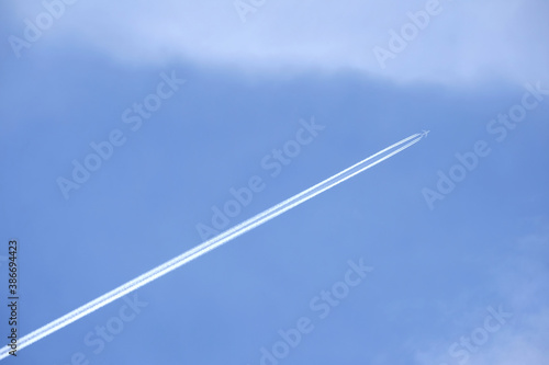 Big passenger supersonic airplane with four jet engines flying high in clear cloudless blue sky, leaving long white trace