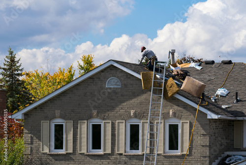 Roofing worker on the roof of a 2-storey family house adding a new layer of asphalt shingles