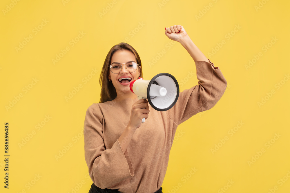 Shouting with megaphone. Portrait of young caucasian woman on yellow studio background with copyspace. Beautiful female model. Concept of human emotions, facial expression, sales, advertising, youth. Shouting with megaphone. Portrait of young caucasian woman on yellow studio background with copyspace. Beautiful female model. Concept of human emotions, facial expression, sales, advertising, youth.