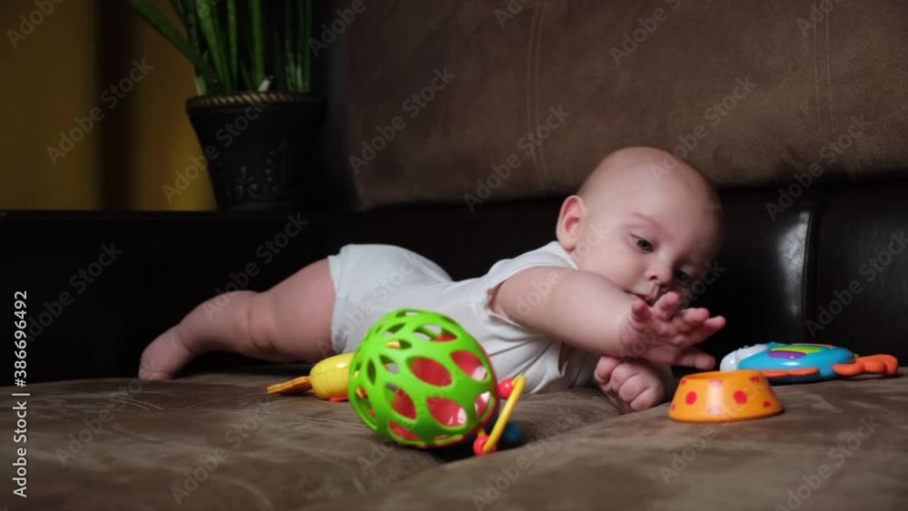 Caucasian infant baby boy playing with plastic developing toys lying on sofa. Caucasian infant baby boy playing with plastic developing toys lying on sofa.