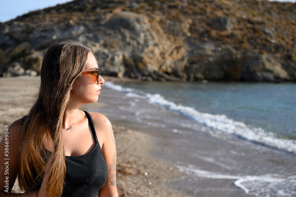 Mujer paseando por la orilla de la playa con ropa negra y gafas de sol