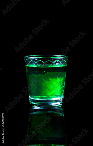 Green liquor in a shot glass with reflection against the black background