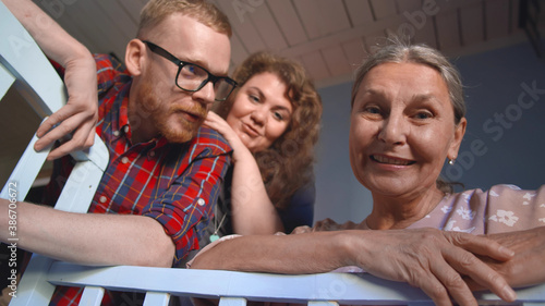 Slika na platnu Bottom view of mother, father and grandmother watching at sleeping baby in cot