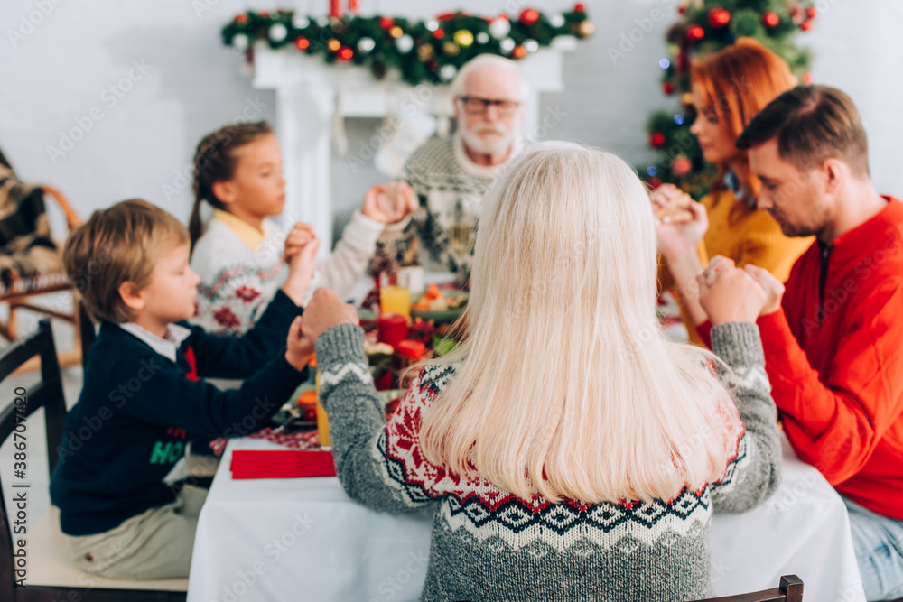 Selective focus of senior woman holding hands with family while sitting at table