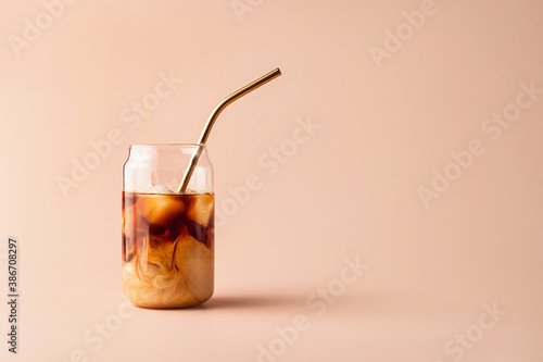 Glass of iced coffee in tall glass with golden straw with cream on pastel background for your design. Food concept in vintage style. Copy space. Closeup.
