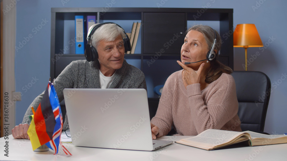 Aged spanish and english teachers in headphones giving online lesson Aged spanish and english teachers in headphones giving online lesson
