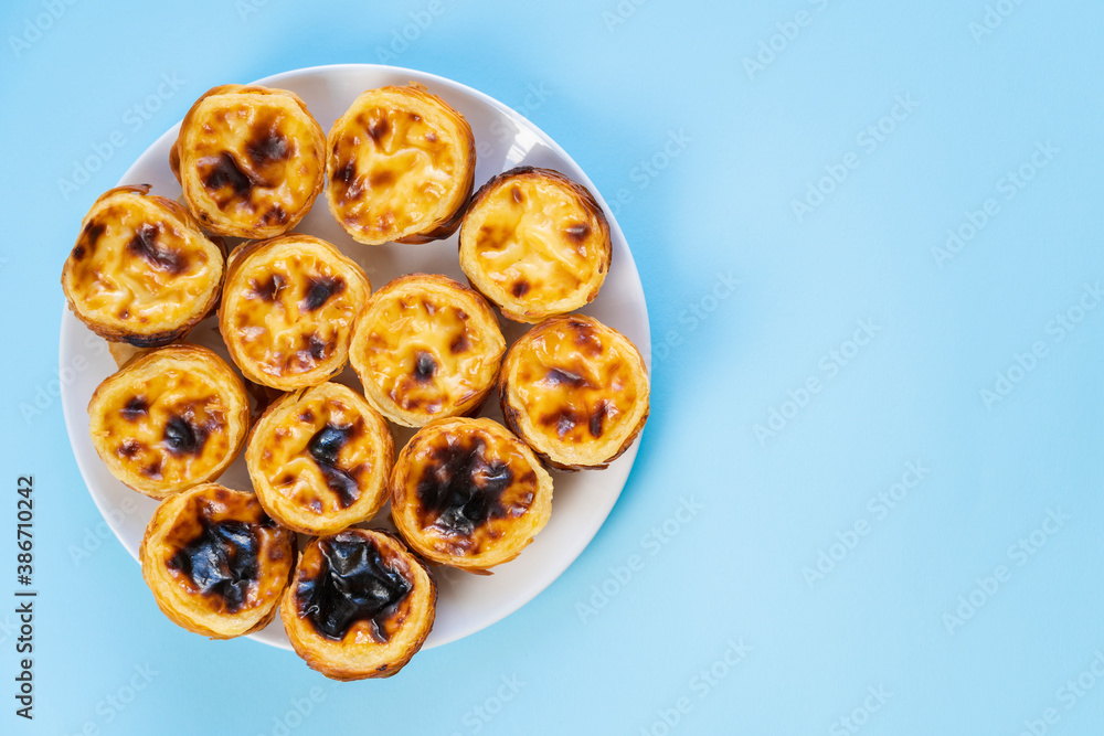 A dozen Pastel de Belem (also called Pasteis de Belem or Portuguese Egg Tarts) on a white plate and light blue background. Food Flat Lay with copy space.