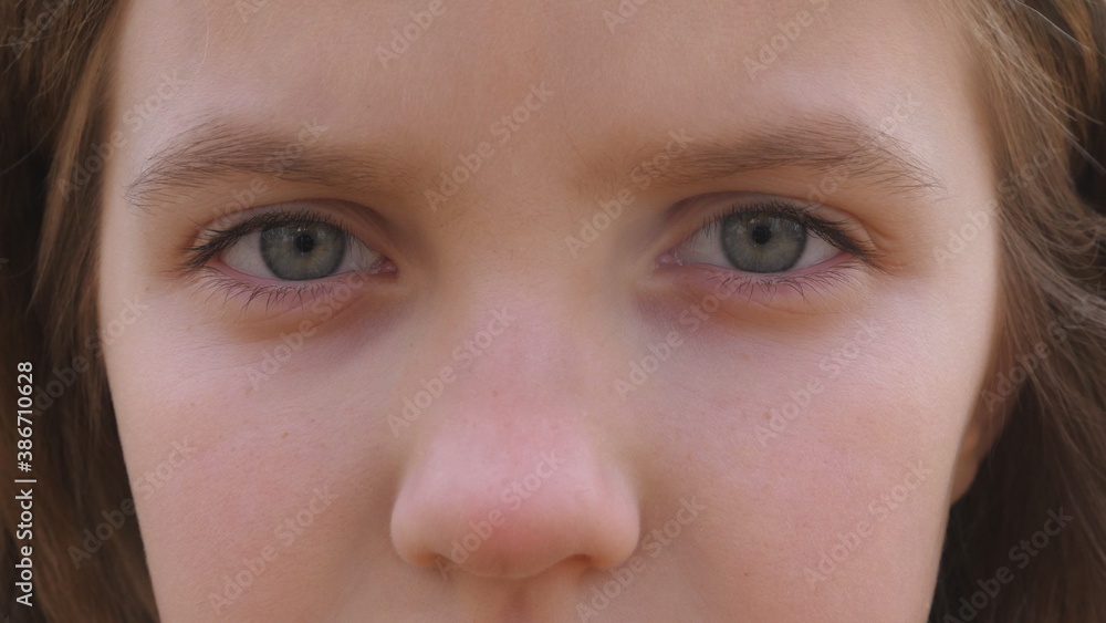 Obraz premium Close up blue eyes of unhappy little blonde girl blinking and looking into camera with a despairing sight. Sorrowful gaze of small depressed child. Facial expression of disappointing female kid
