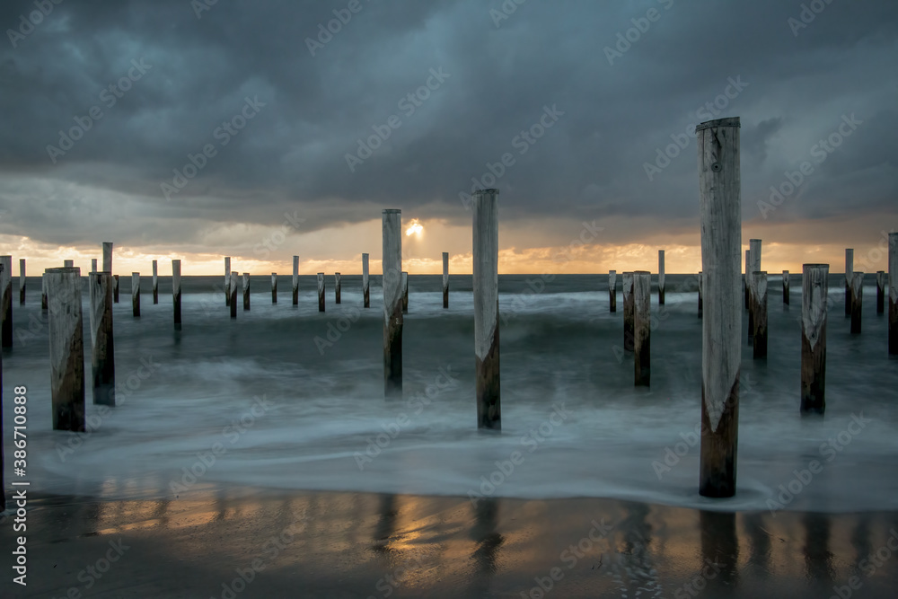 LONG EXPOSURE PHOTOGRAPHY, taken at the North Sea in Petten with the pole village in the sea, taken during the evening hours with a beautiful setting orange sun and heavy clouds.