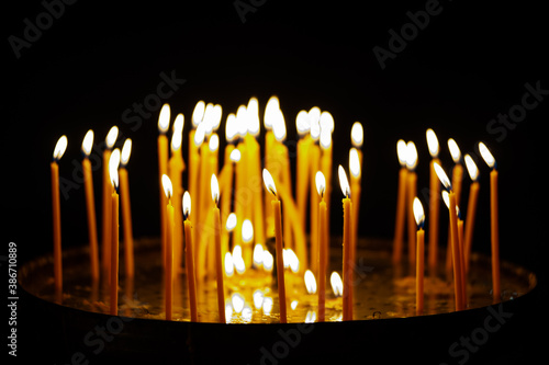 Many wax candles on a tray in the church are burning