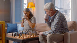 Happy senior couple resting at home drinking coffee and playing chess