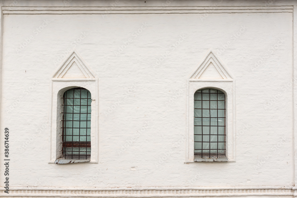 Elegant facade of historical building arch windows with rusty metal grids and foil on white painted wall on summer day. Traditional architectural style