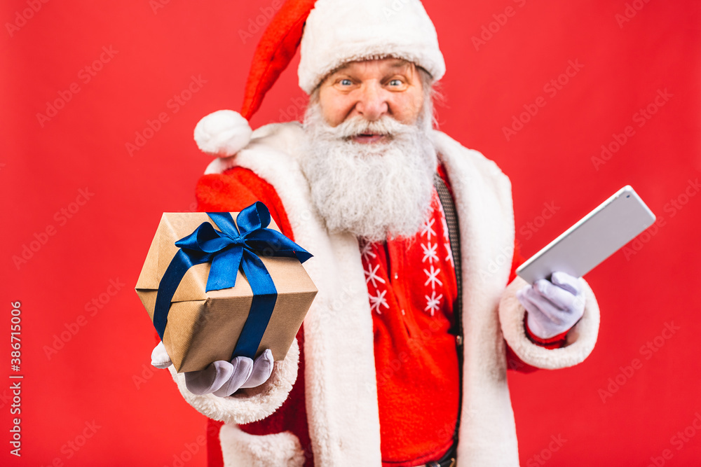 Naklejka premium Santa Claus standing isolated on red background. Christmas and new year concept. Using tablet computer.