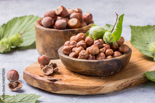 Hazelnuts with peeled hazelnut and leaf in brown bowl on concrete background.