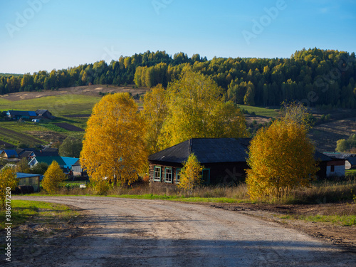 Old abandoned dilapidated village house by the road, autumn landscape.