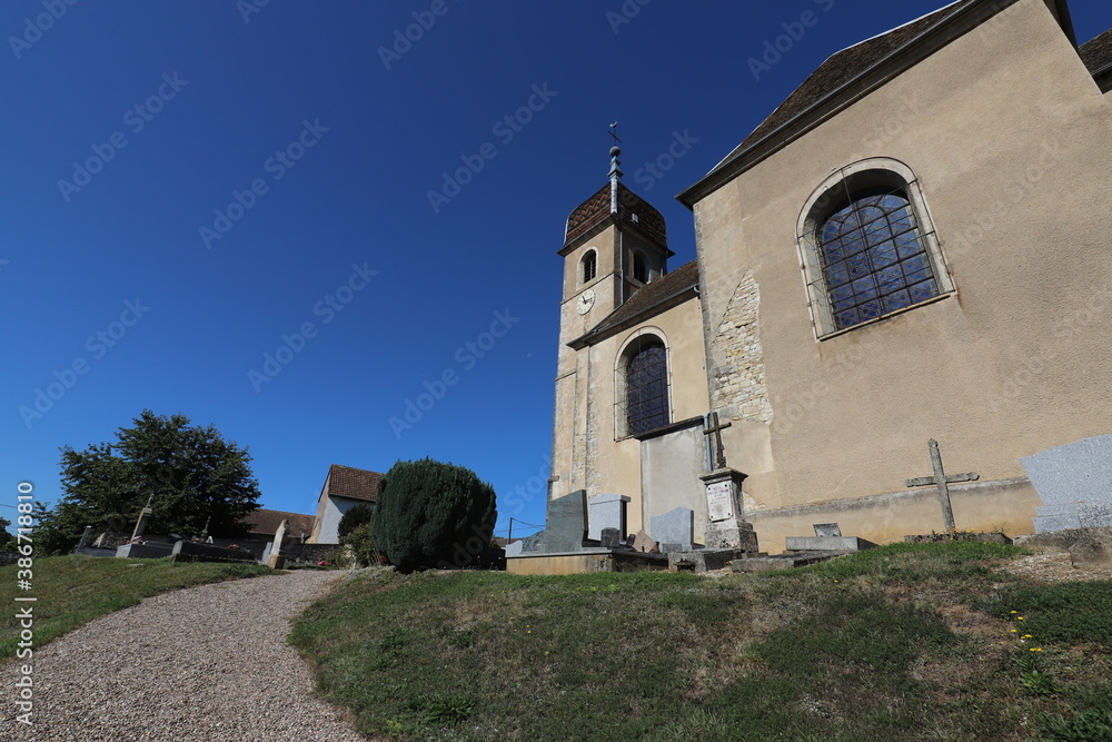 Fototapeta premium Beautiful characteristic small cemetery next to a village church in France. Photo is taken on a warm summer with a blue sky.