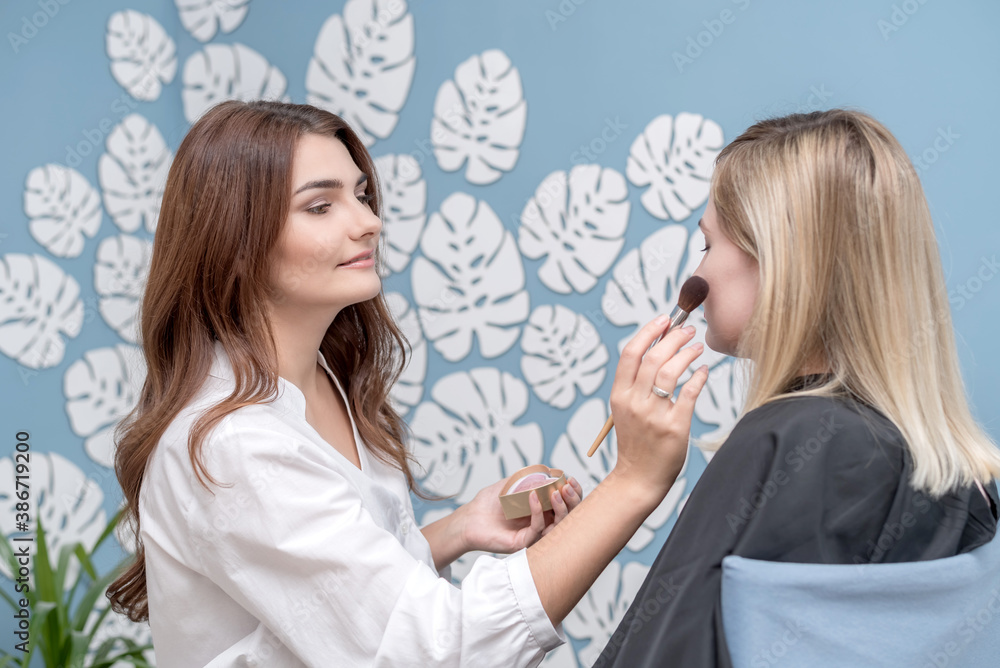 Beautiful young make-up artist makes makeup to a young blonde. Beautiful young make-up artist makes makeup to a young blonde.