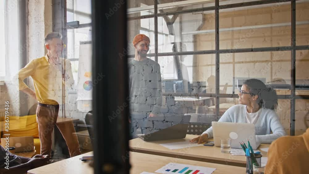 Informal business meeting. View through glass wall at young positive team discussing projects, tracking shot Informal business meeting. View through glass wall at young positive team discussing projects, tracking shot