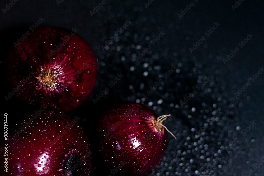 Three heads of fresh red-purple onions in the lower left corner. Drops of moisture on the peel. Three heads of fresh red-purple onions in the lower left corner. Drops of moisture on the peel.