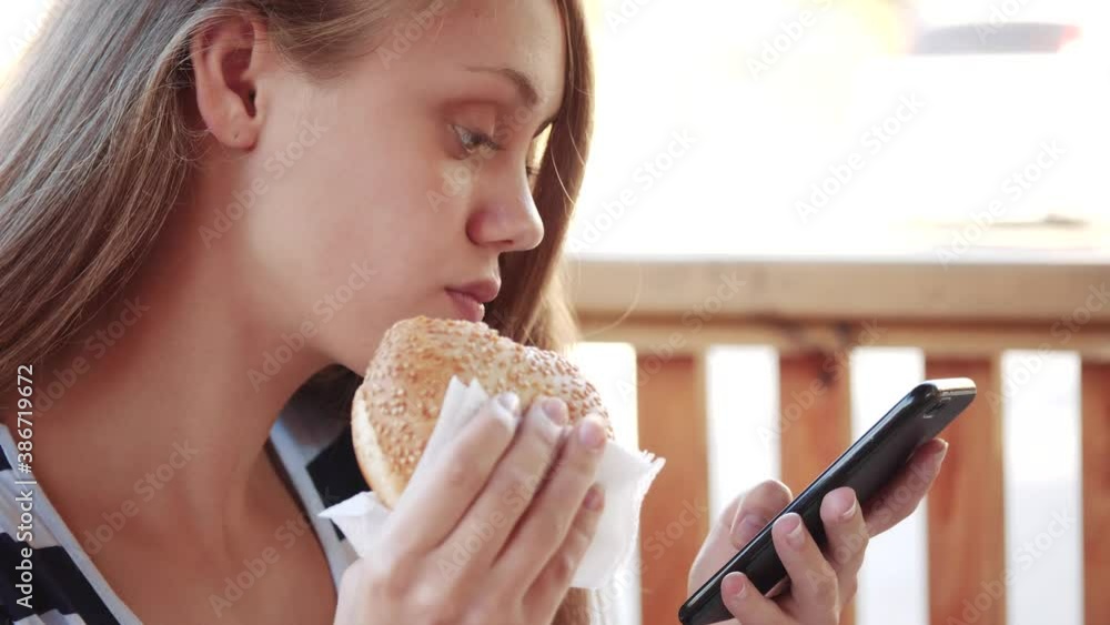 girl eating a sandwich close-up looking into a smartphone. fast food concept. teenager eats fast food in cafe watching social networks. girl eating a sandwich looks into lifestyle a smartphone