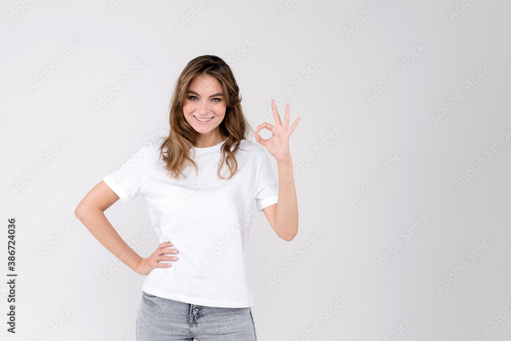 Happy millennial woman looking at camera, showing ok gesture, isolated on white studio background. Smiling female customer agree with good deal, young employee accepting job offer. Empty space