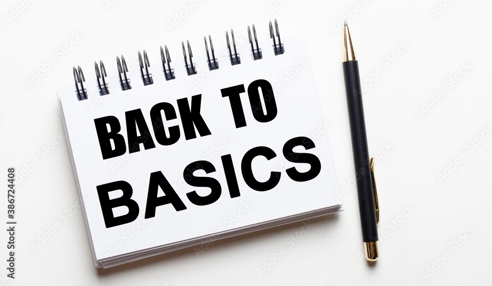 On a light background, a white notebook with the words BACK TO BASICS and a pen. On a light background, a white notebook with the words BACK TO BASICS and a pen.