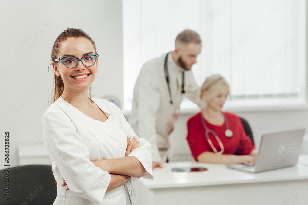 A brunette female doctor in uniform, smiling and posing at camera, behind her on the background two other doctors A brunette female doctor in uniform, smiling and posing at camera, behind her on the background two other doctors