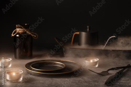 Vintage template with old metal tablewareand lit candles on black stone background for concept design. Fall concept. Interior design concept.