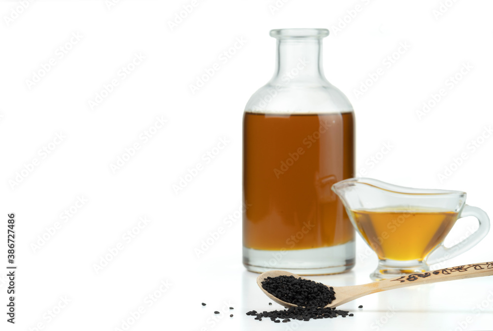 A handful of black cumin seeds on the background of a glass gravy boat and a bottle with black seed oil. Isolated on white. A handful of black cumin seeds on the background of a glass gravy boat and a bottle with black seed oil. Isolated on white.