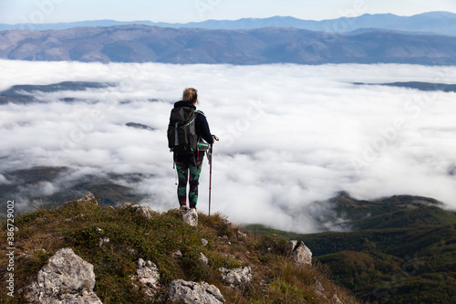 Girl, mountain hiker with walking sticks above clouds from Suva planina (Dry mounain)