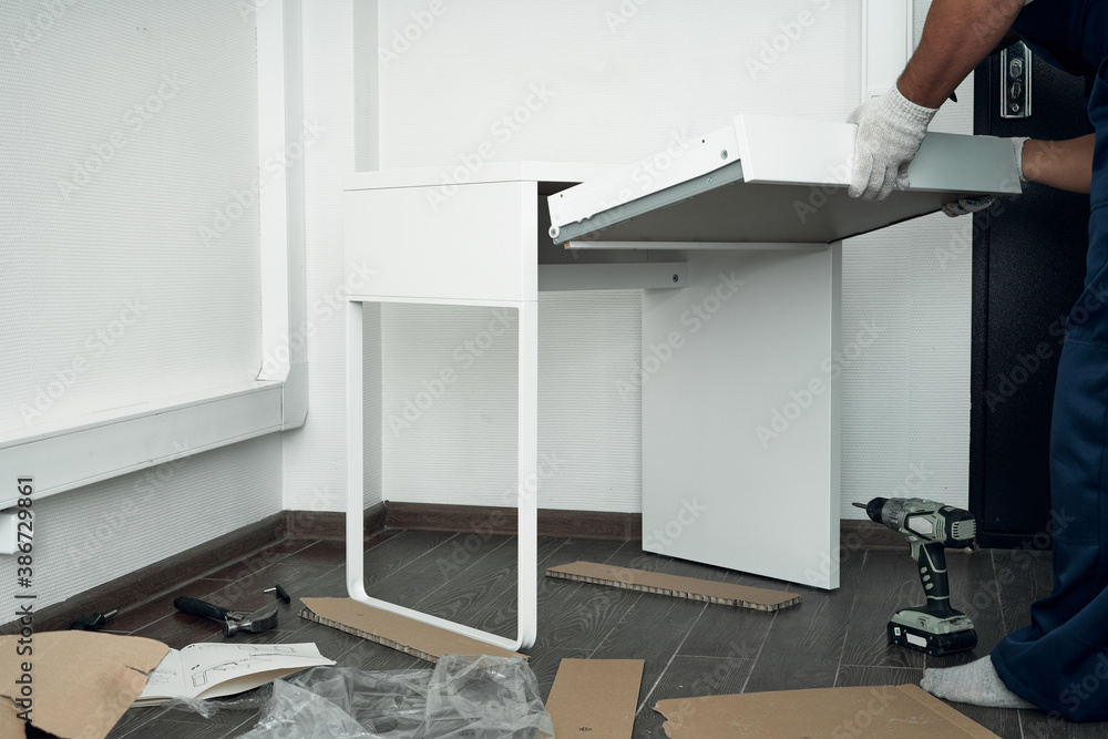 Furniture assembly process. Worker in overalls and white footwear. Installation of a drawer. Do it yourself. Furniture assembly process. Worker in overalls and white footwear. Installation of a drawer. Do it yourself.