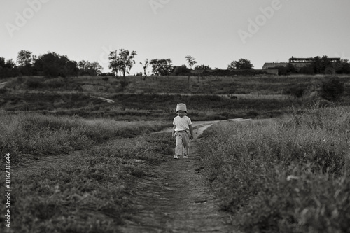 Two-year-old child in a hat walks along a country road, summer. Knowledge of the world. Black and white photo