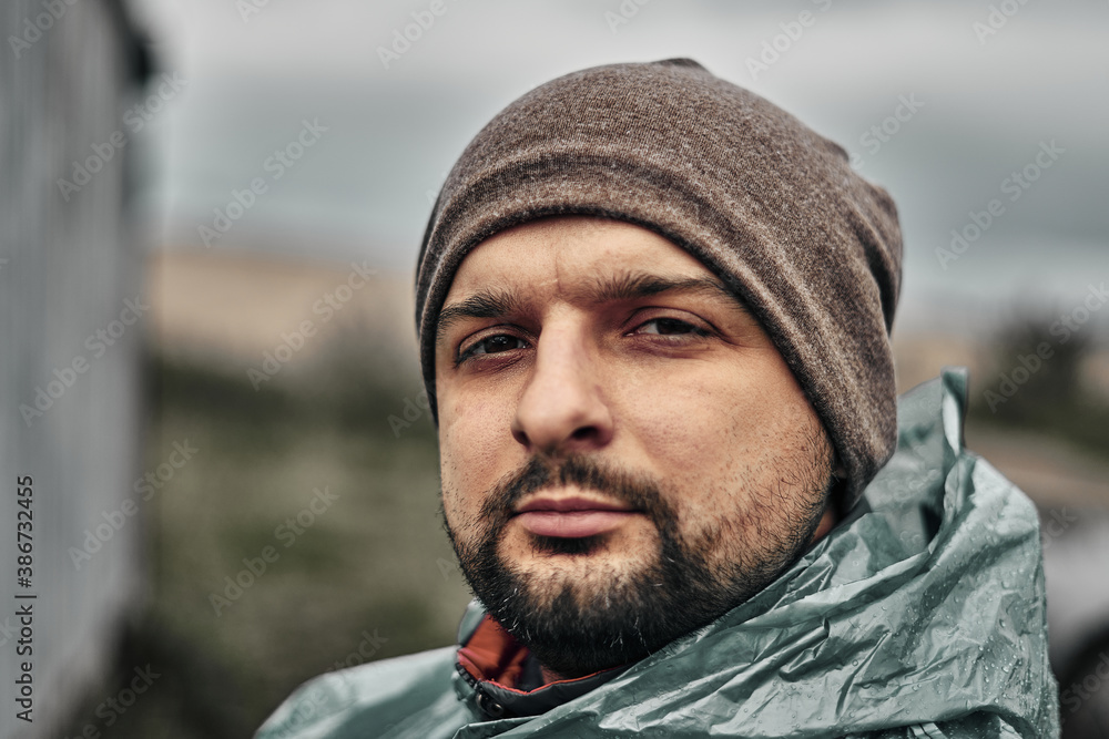 A man with a beard in a green raincoat and hat, face close-up. Overcast weather. A man with a beard in a green raincoat and hat, face close-up. Overcast weather.