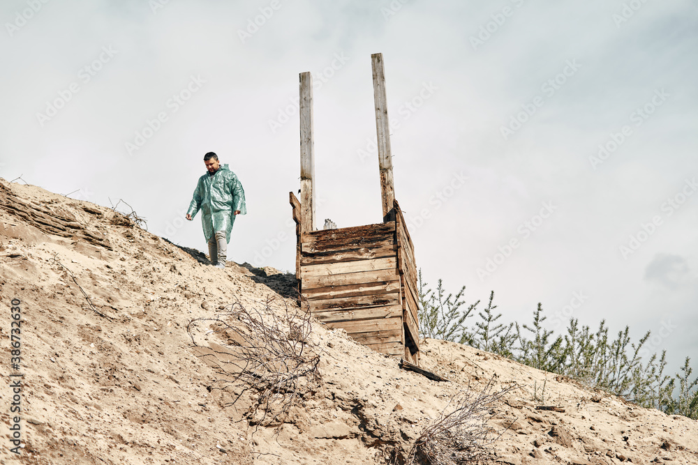 Abandoned wooden well on the sand and a man near the well in a raincoat, cloudy sky. Research of abandoned places. Abandoned wooden well on the sand and a man near the well in a raincoat, cloudy sky. Research of abandoned places.