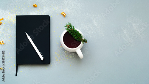 Christmas grey background with sparkles. White ceramic cup with tea and Goal-setting notebook. Planning concept. Creative copy space.