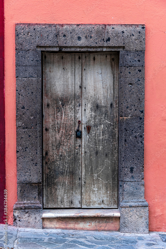 old faded grey wooden door in a dark grey stone frame and a pink wall